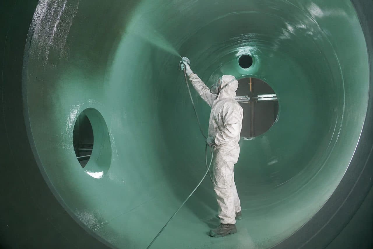 F+G Techniker im Schutzanzug beschichtet das Innere eines großen Tanks im Spritzverfahren